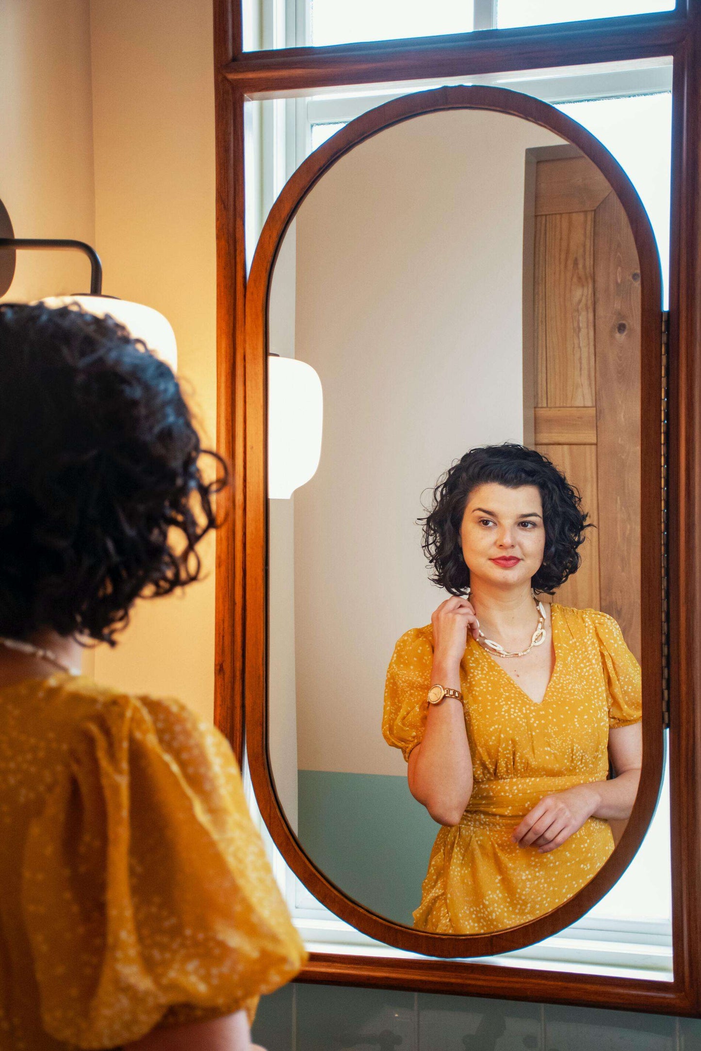 a girl wears hypoallergenic earrings in front of mirror