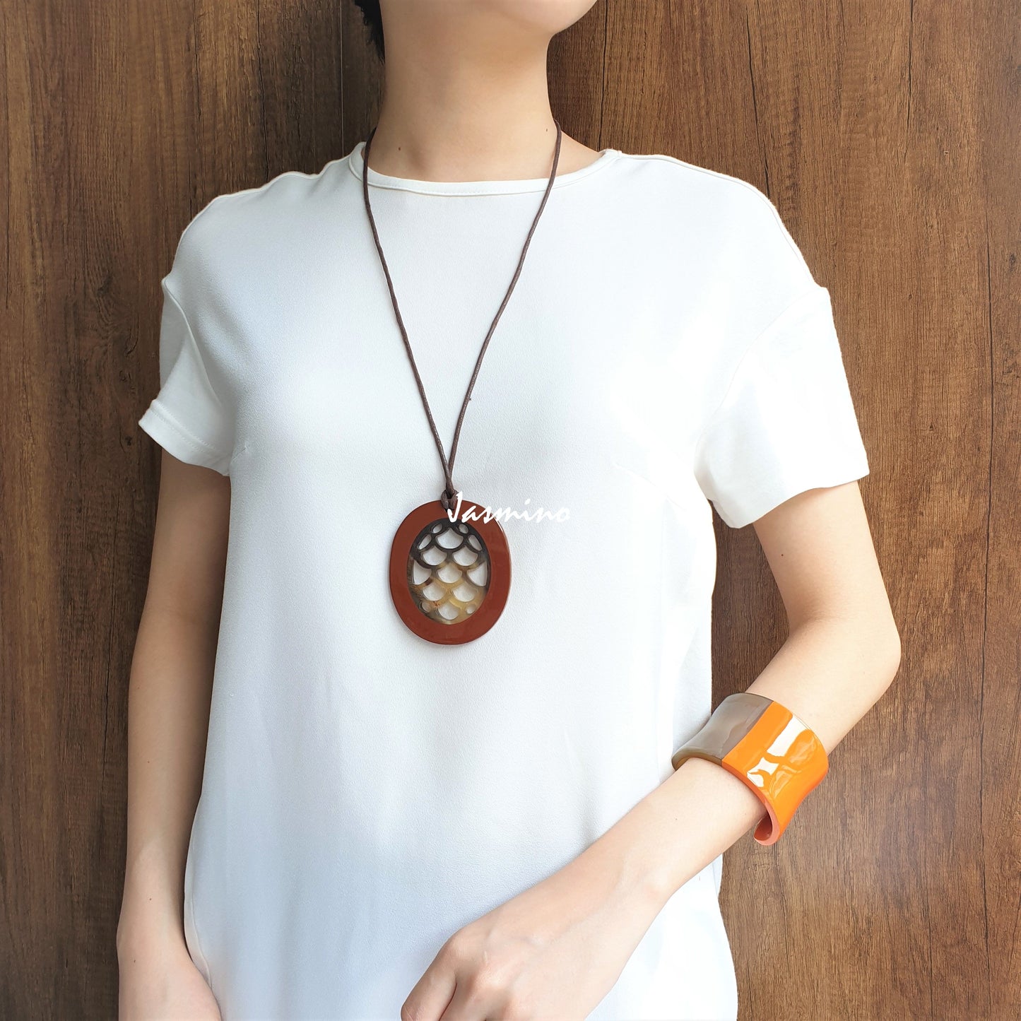 A model is wearing Jasmino unique handmade mermaid orange pendant is shaped by an oval made of natural buffalo horn for women's gifts