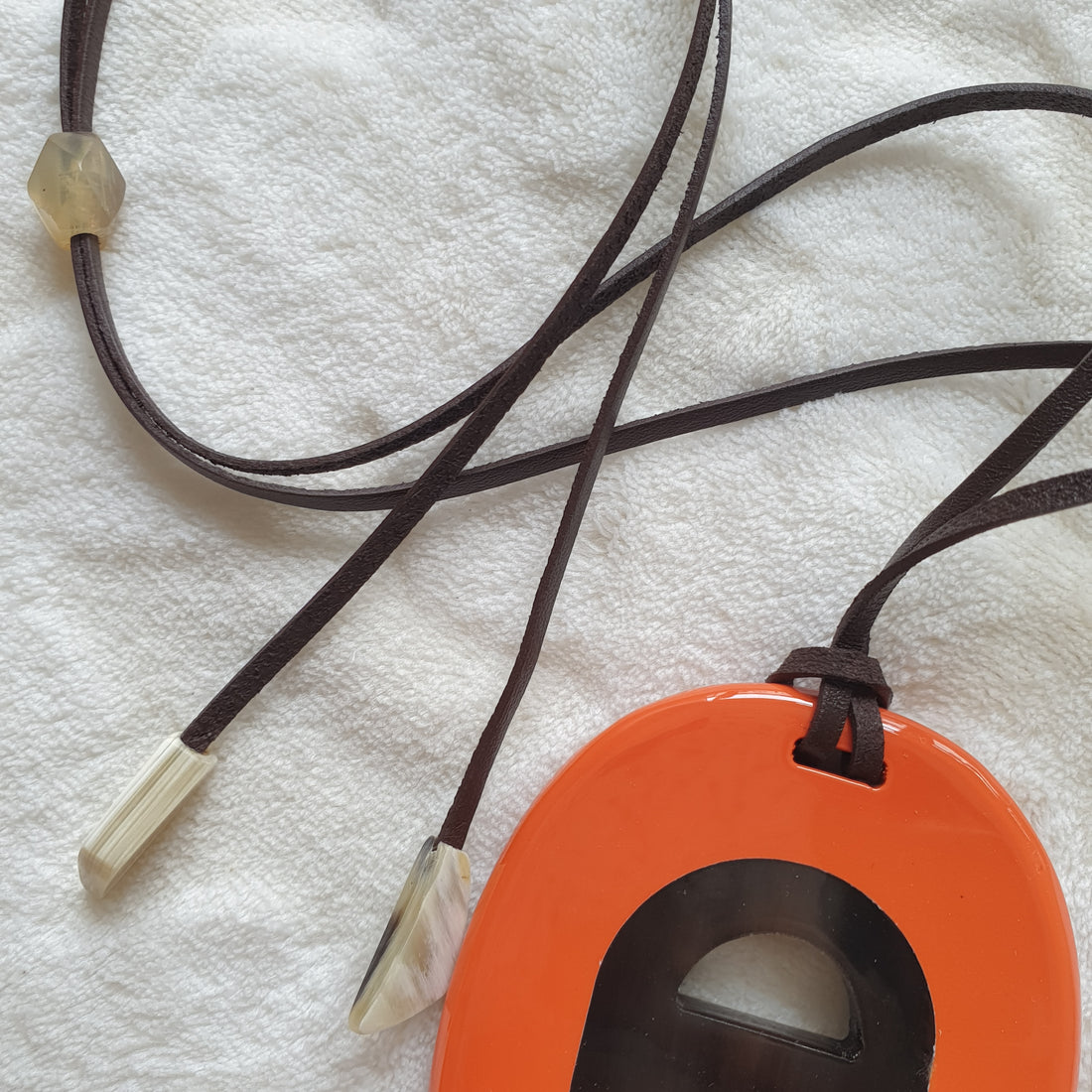 orange lacquer pendant with suede brown cord on the light background, impressive gift for her