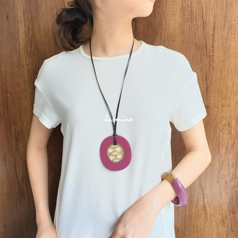 
                  
                    A model is wearing unique handmade Vintage oval pendant has a pink outline in natural buffalo horn for women in the natural light
                  
                