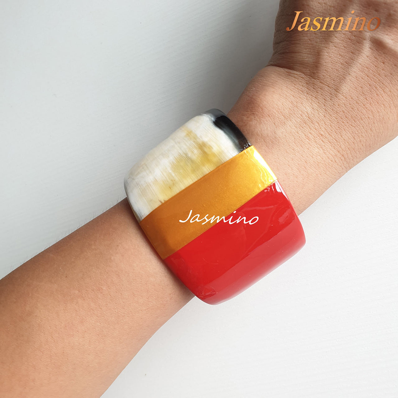 A model is wearing Jasmino unique handmade cuff bracelet features brown, red, and yellow in natural buffalo horn for women on Christmas gifts