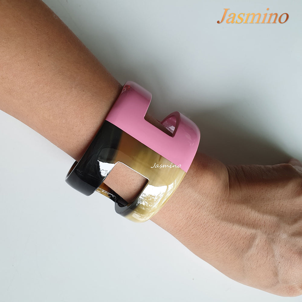 
                  
                    A handmade cuff bracelet is shaped by "H" letter with natural buffalo horn material and a blush pink on a white background
                  
                