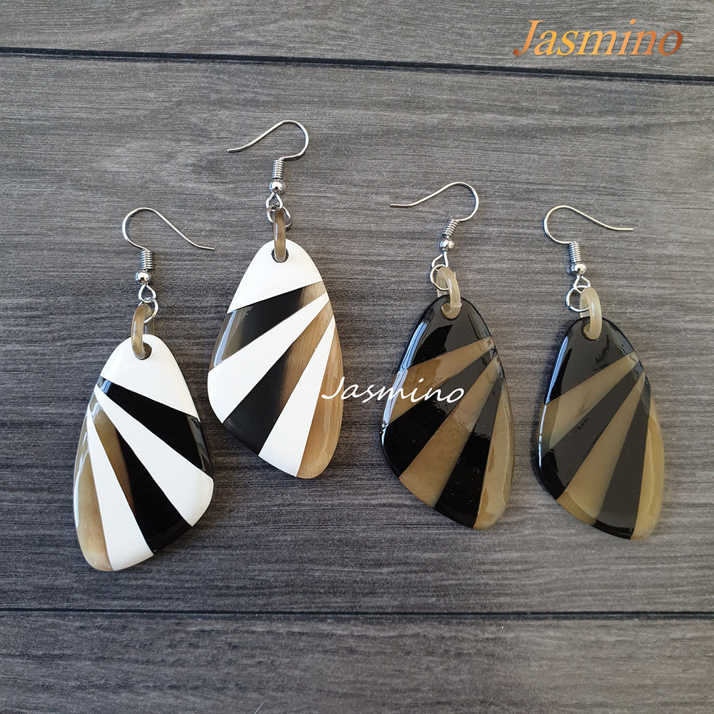 
                  
                    Two pairs of handmade dangle earrings are amber, black, yellow, and whilte color on a dark background
                  
                