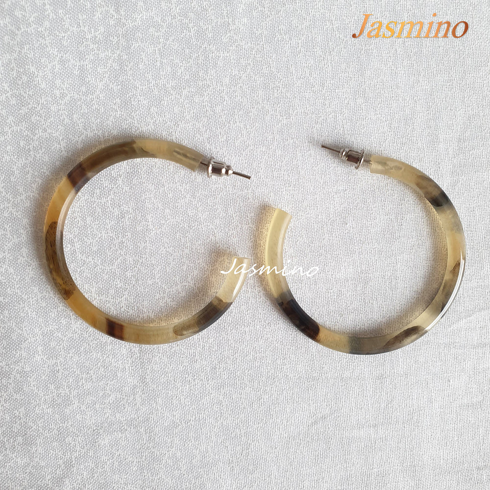 
                  
                    Handmade C-shaped hoop earrings feature a mix of brown and yellow color and natural horn on the light background
                  
                