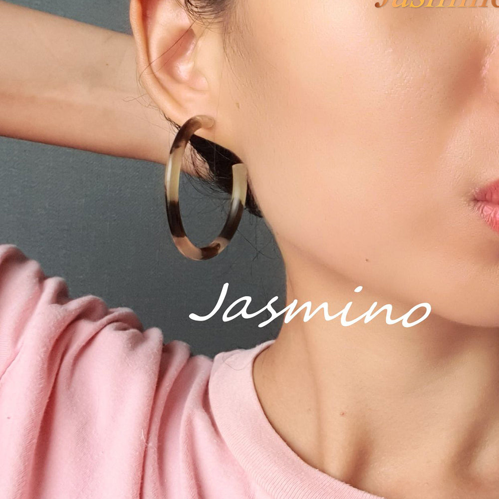 
                  
                    Handmade C-shaped hoop earrings feature a mix of brown and yellow color and natural horn worn by a woman in the natural light
                  
                