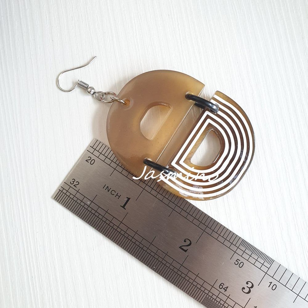 
                  
                    Handmade D-shaped dangle earrings feature brown and white color in the natural light
                  
                