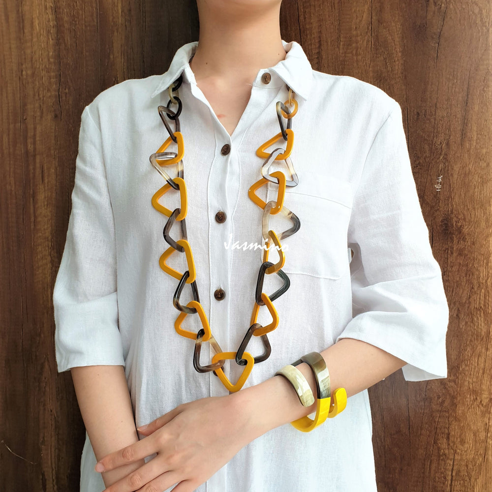 
                  
                    A girl is wearing yellow lacquered triangular pieces and a snake cuff bracelet in the natural light
                  
                