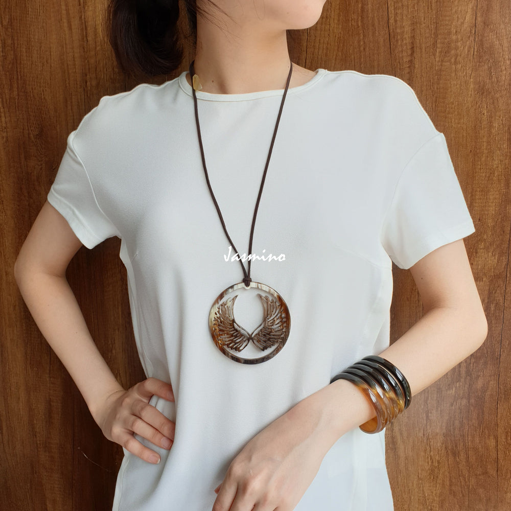 
                  
                    A women is wearing Jasmino Vintage angle wing circle pendant features a dark and light colour that is made of natural buffalo horn for men and women
                  
                