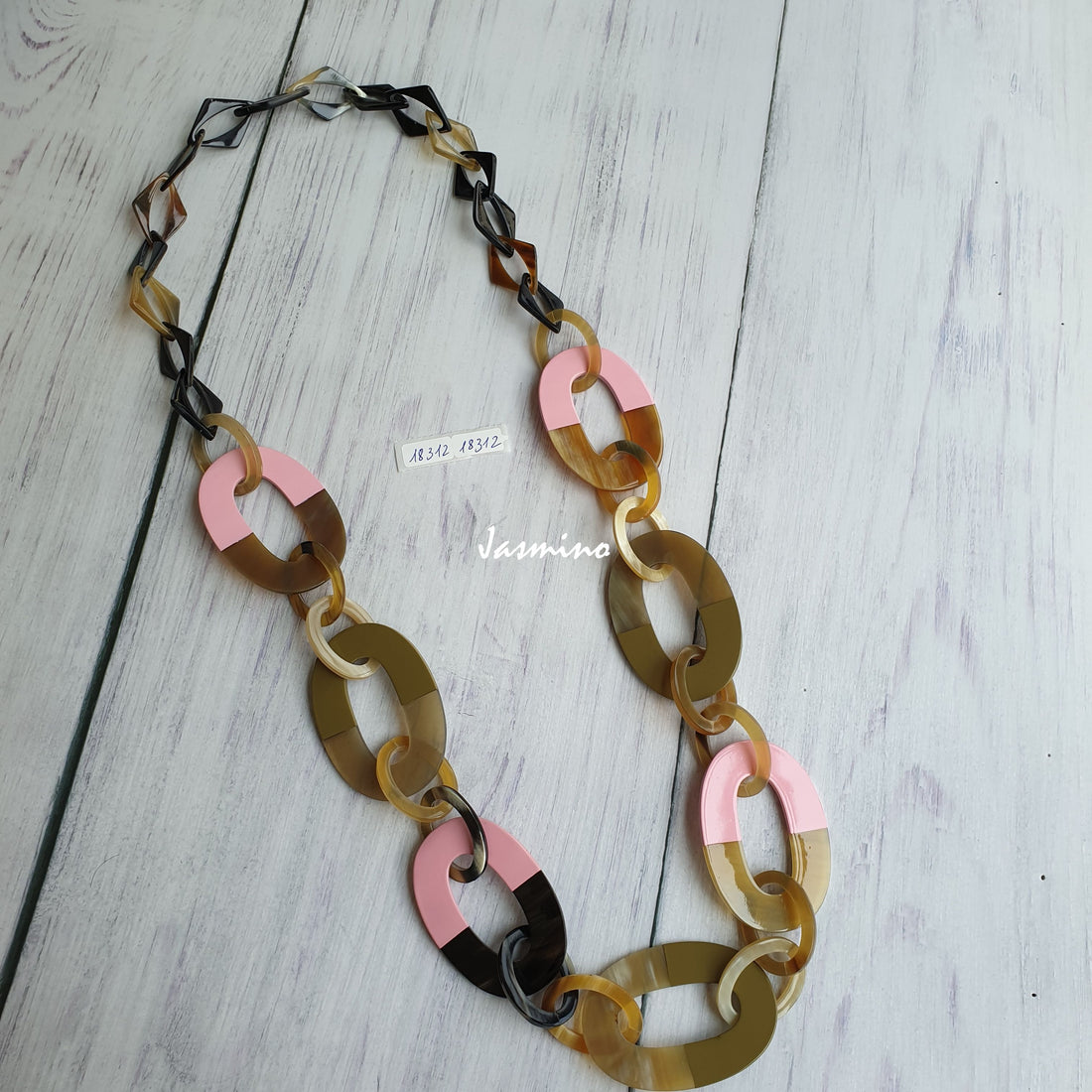 A handmade wide chain necklace features a mix of brown, black, and pink color on a white floor