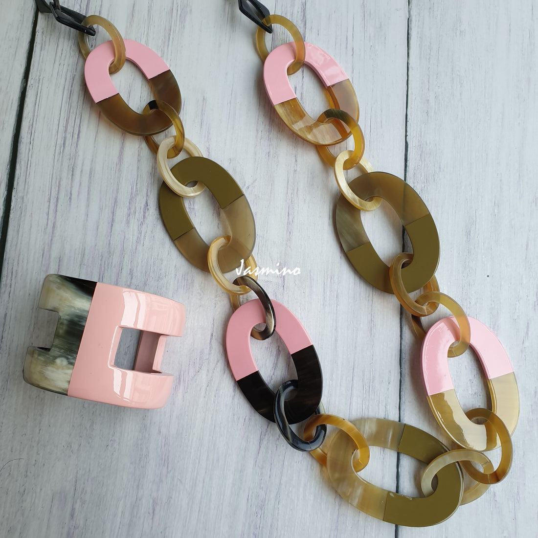  A collection of a pink wide chain necklace and cuff bracelet is made by natural buffalo horn on a white floor