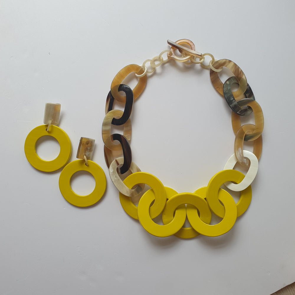 
                  
                    A collection of solid yellow circle earrings and a wide chain necklace on a white background
                  
                