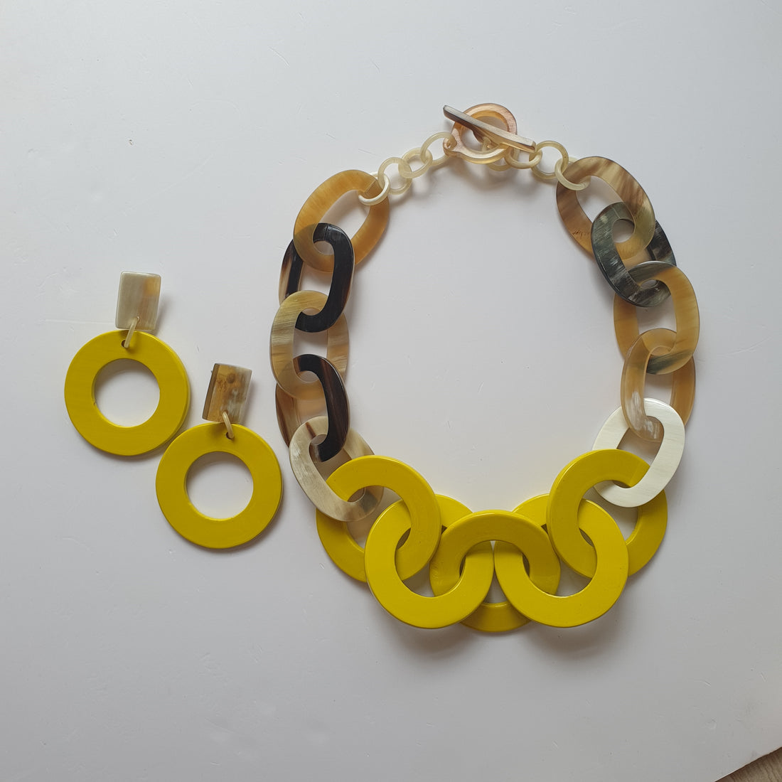 A collection of solid yellow circle earrings and a wide chain necklace on a white background