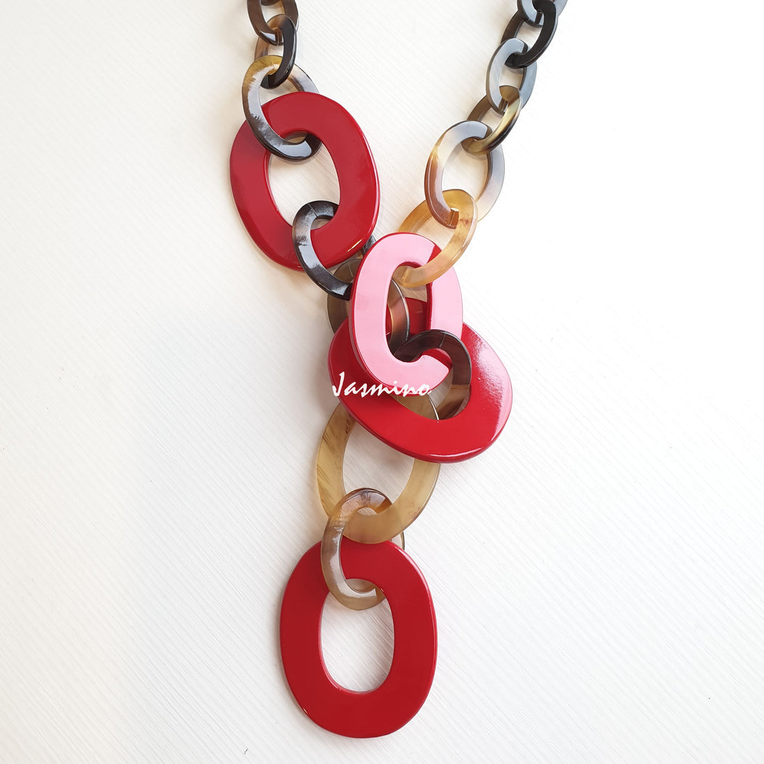 A wide chain necklace features natural buffalo horn and red color on a white background